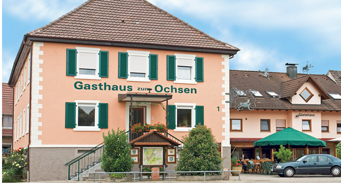 Fassade des Gasthauses Zum Ochsen, ein pfirsichfarbenes Haus mit grünen Fensterläden und dem Schriftzug Gasthaus zum Ochsen