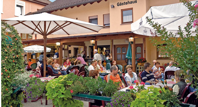 Biergarten und Terrasse des Gasthauses mit Gästen unter Sonnenschirmen